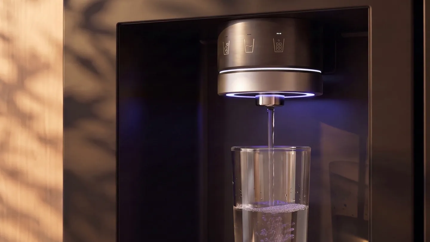 A frame of the film: water pours from a refrigerator's dispenser into a glass, in warm afternoon light with leaf shadows on the door.