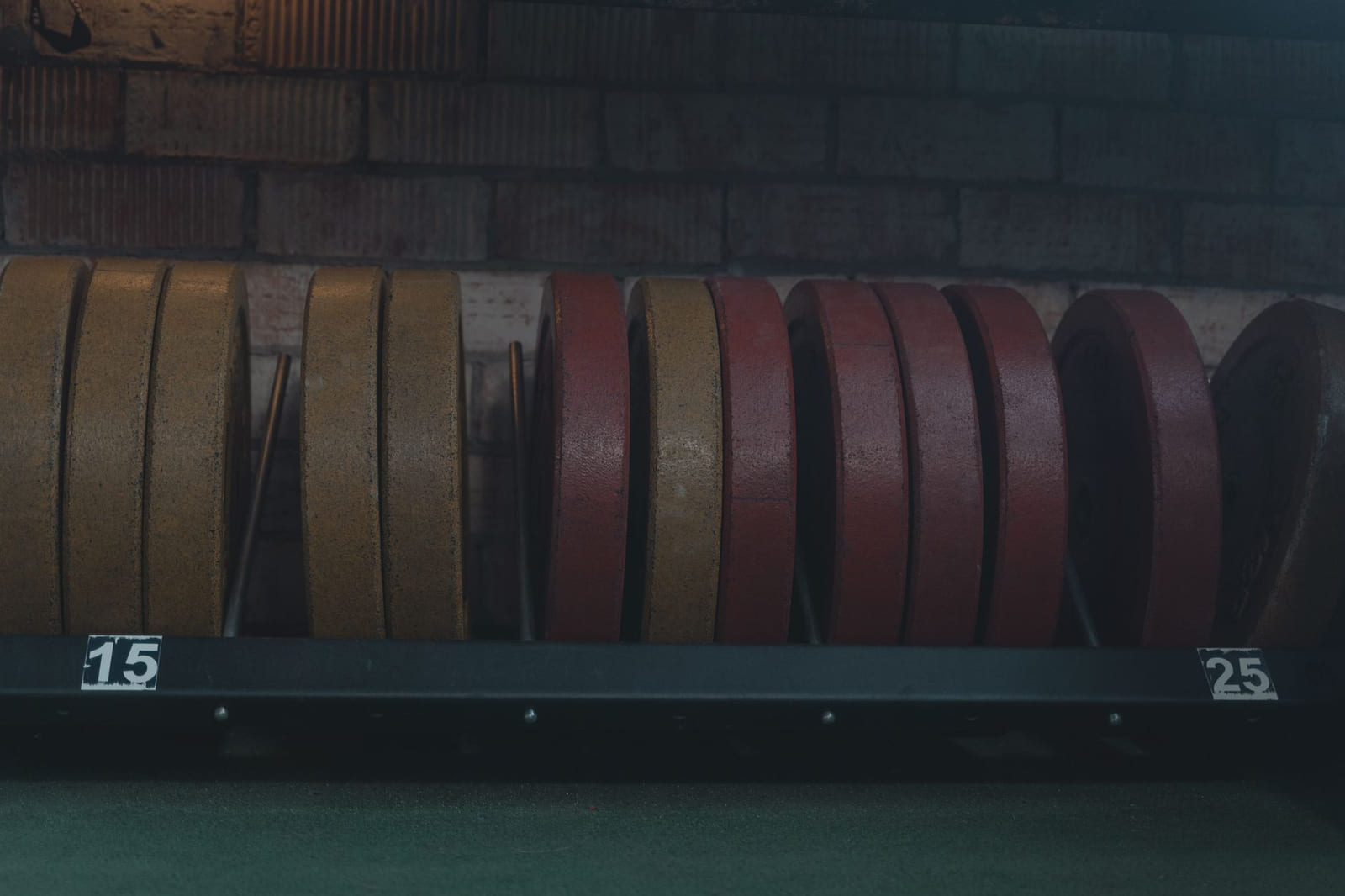 A rack of old painted iron plates against a brick wall, with stencilled weight labels.