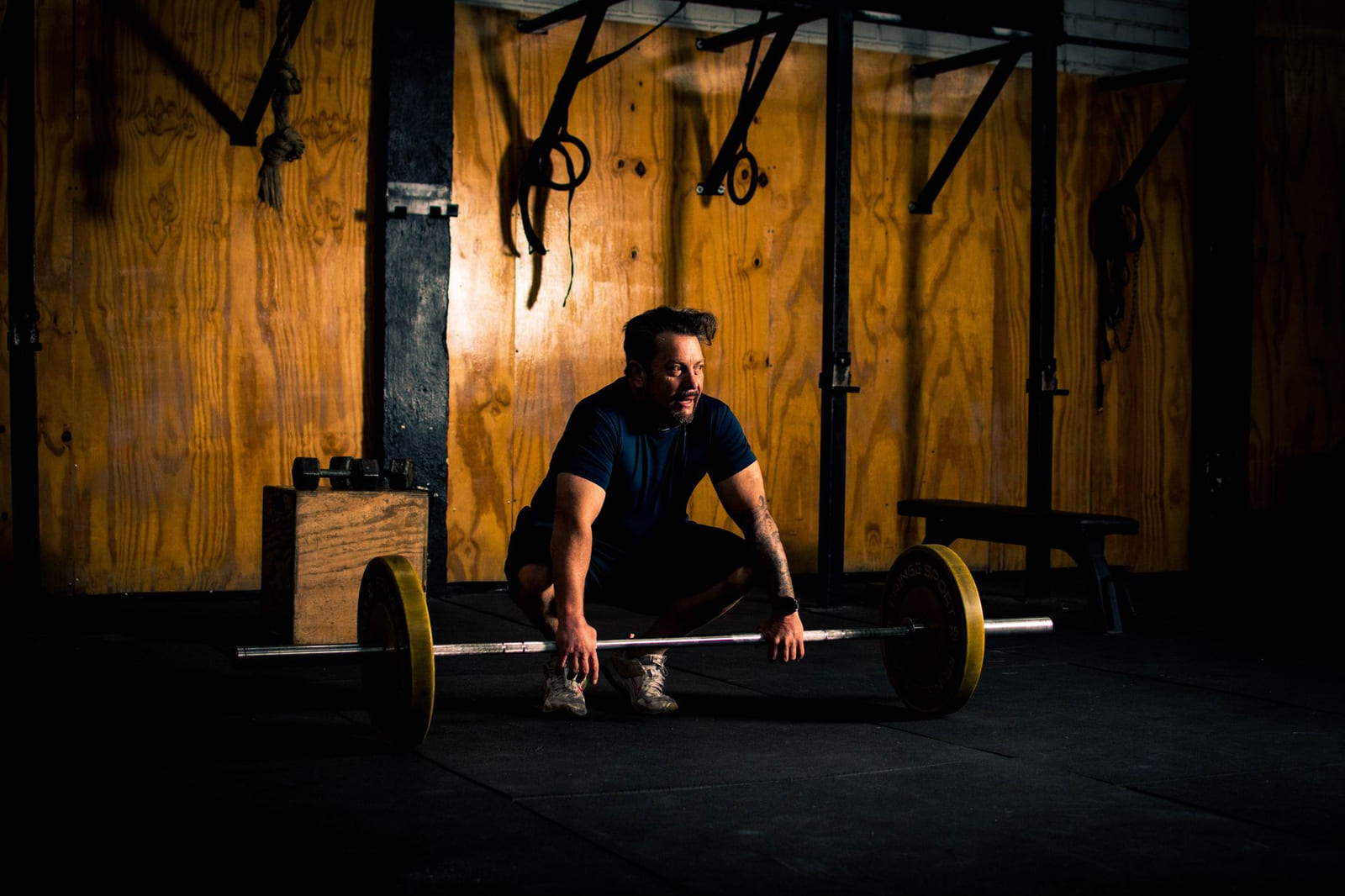 The lifting floor at Iron Island Barbell: a loaded barbell on the platform, plywood walls, rings and a plyo box behind it.