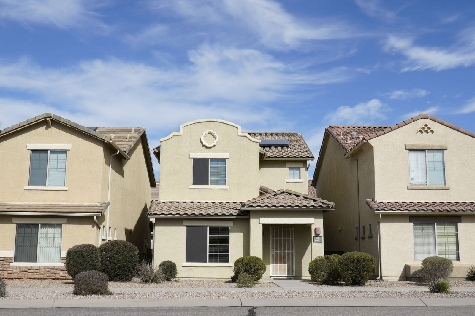 A quiet residential street in west Phoenix at midday: single-storey houses, gravel front yards, and condenser units at the side of every house.