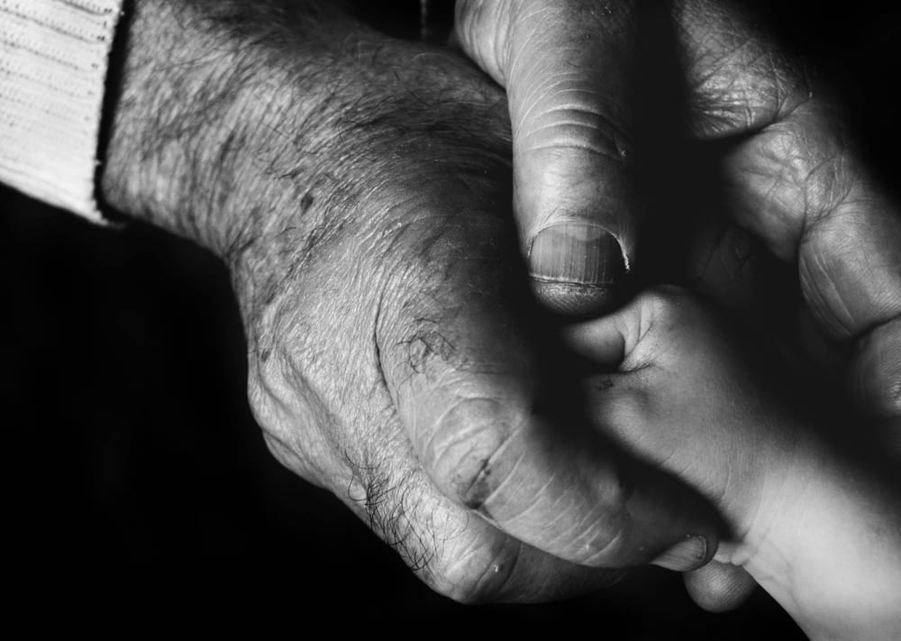 An elderly hand holding a child's hand, photographed close up in black and white.
