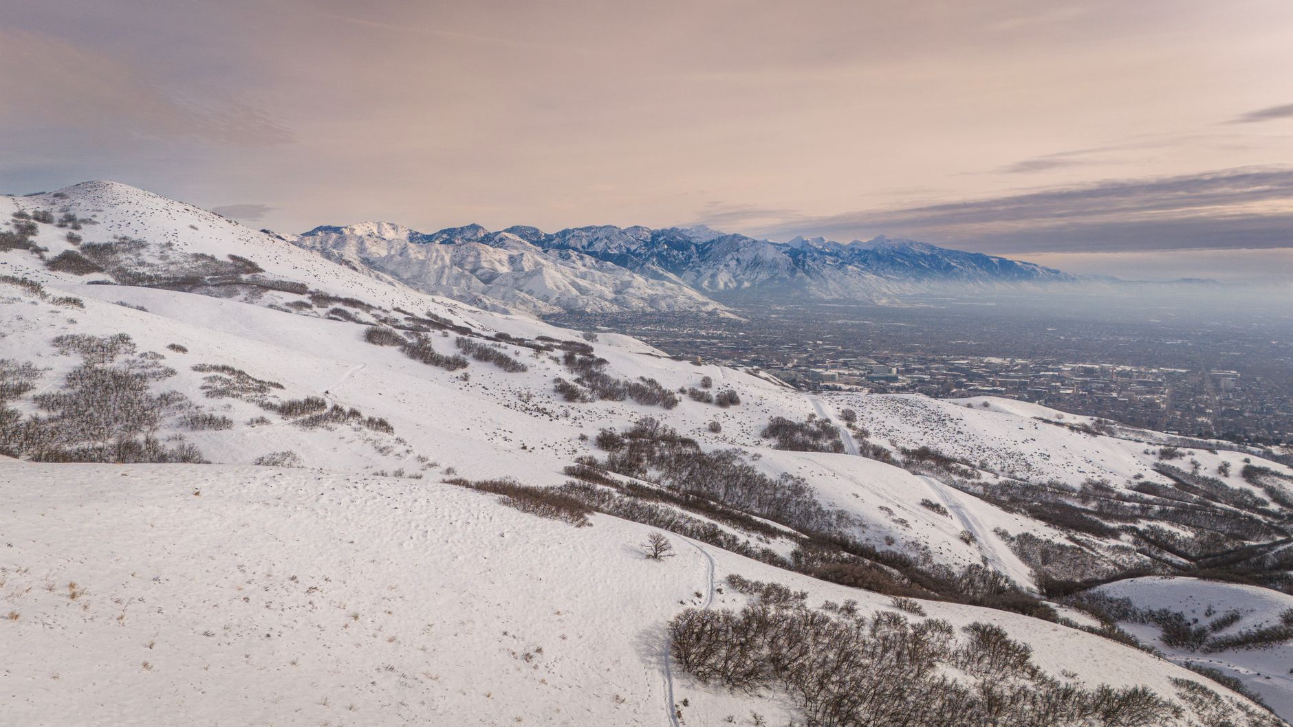 The Salt Lake valley seen from the snow-covered foothills in winter, the Wasatch range running across the horizon.