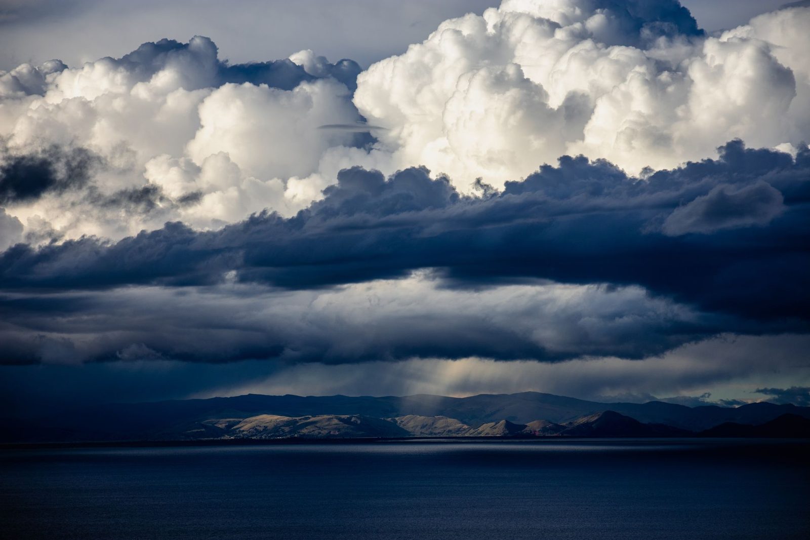Storm clouds over Lake Titicaca, a shaft of light falling on the hills of the shore