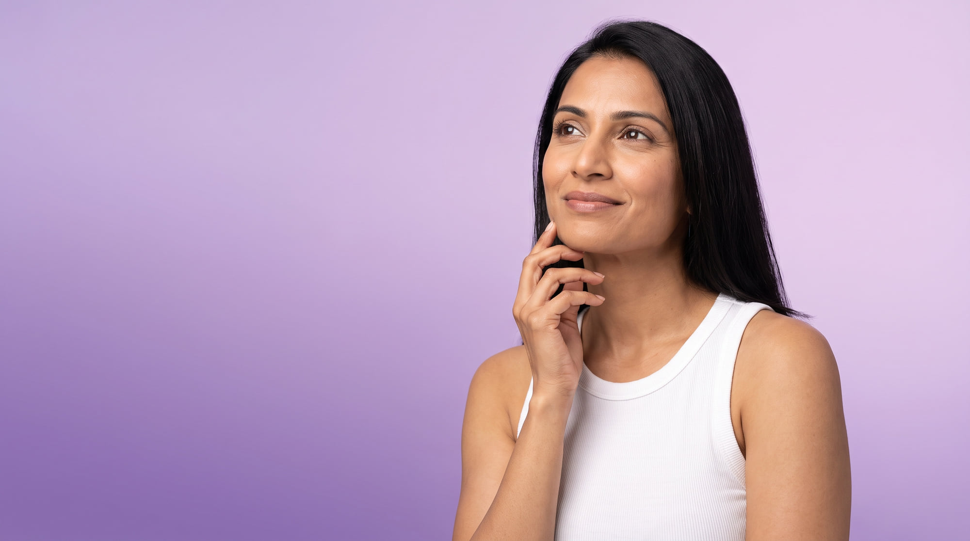 A woman in her thirties looking up with a small smile, on a lilac background.