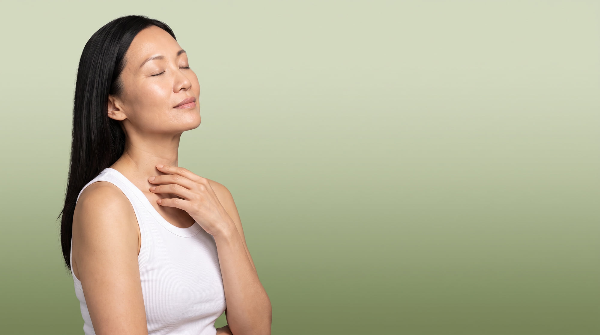 A woman in her forties with her eyes closed and her face tilted to the light, on a sage green background.
