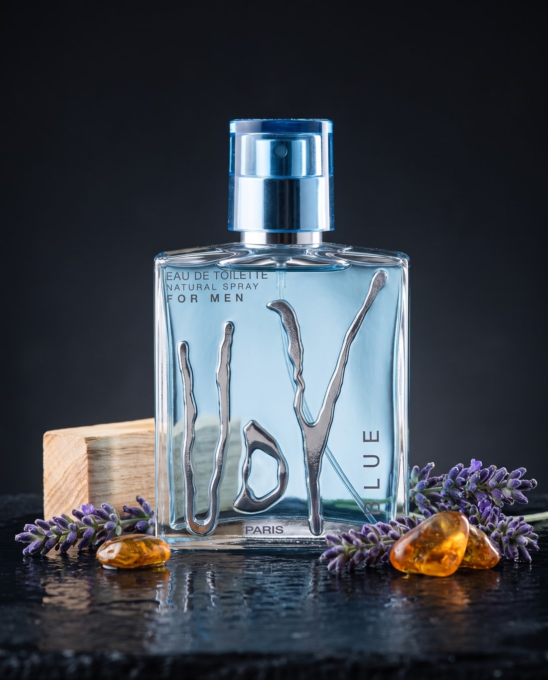 UDV Blue beside lavender in bud, a block of pale wood and pieces of amber resin on wet slate.